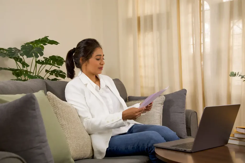 woman with laptop and documents sitting at home on couch