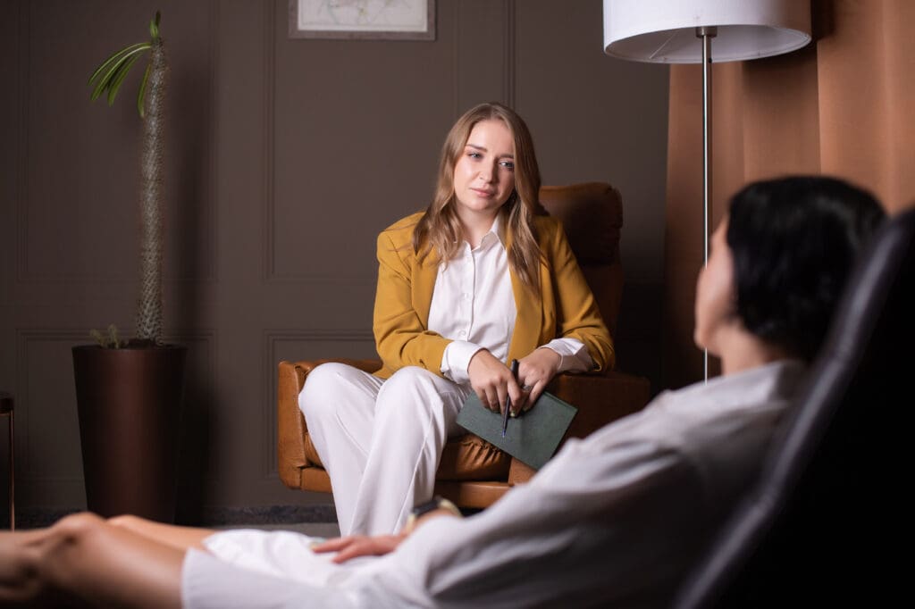 A female psychologist sits in a chair and listens to a client